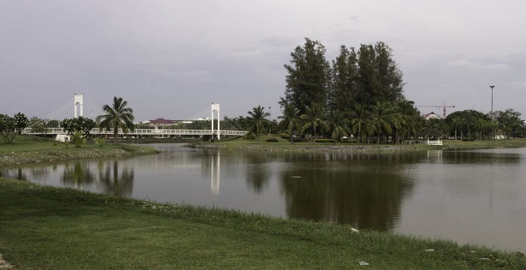ผืนน้ำหนองประจักษ์ มีสะพานแขวนสีขาวและแนวต้นไม้ริมทะเลสาบ