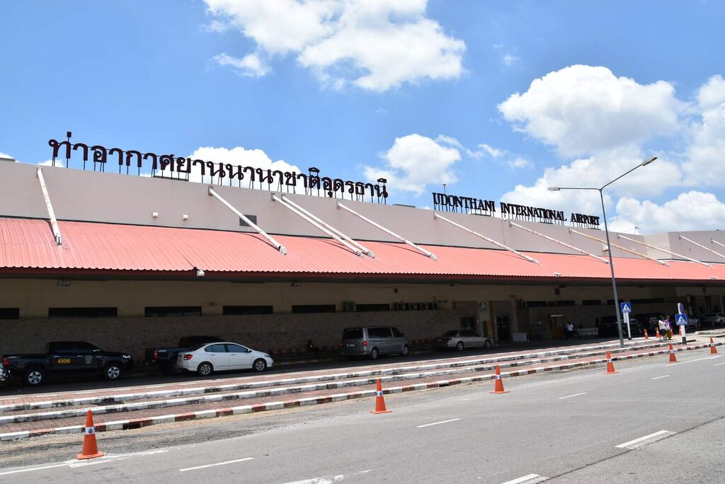 ด้านหน้าอาคารผู้โดยสารท่าอากาศยานนานาชาติอุดรธานี มีป้ายชื่อสนามบินภาษาไทยและอังกฤษ และรถจอดริมทางเท้า
